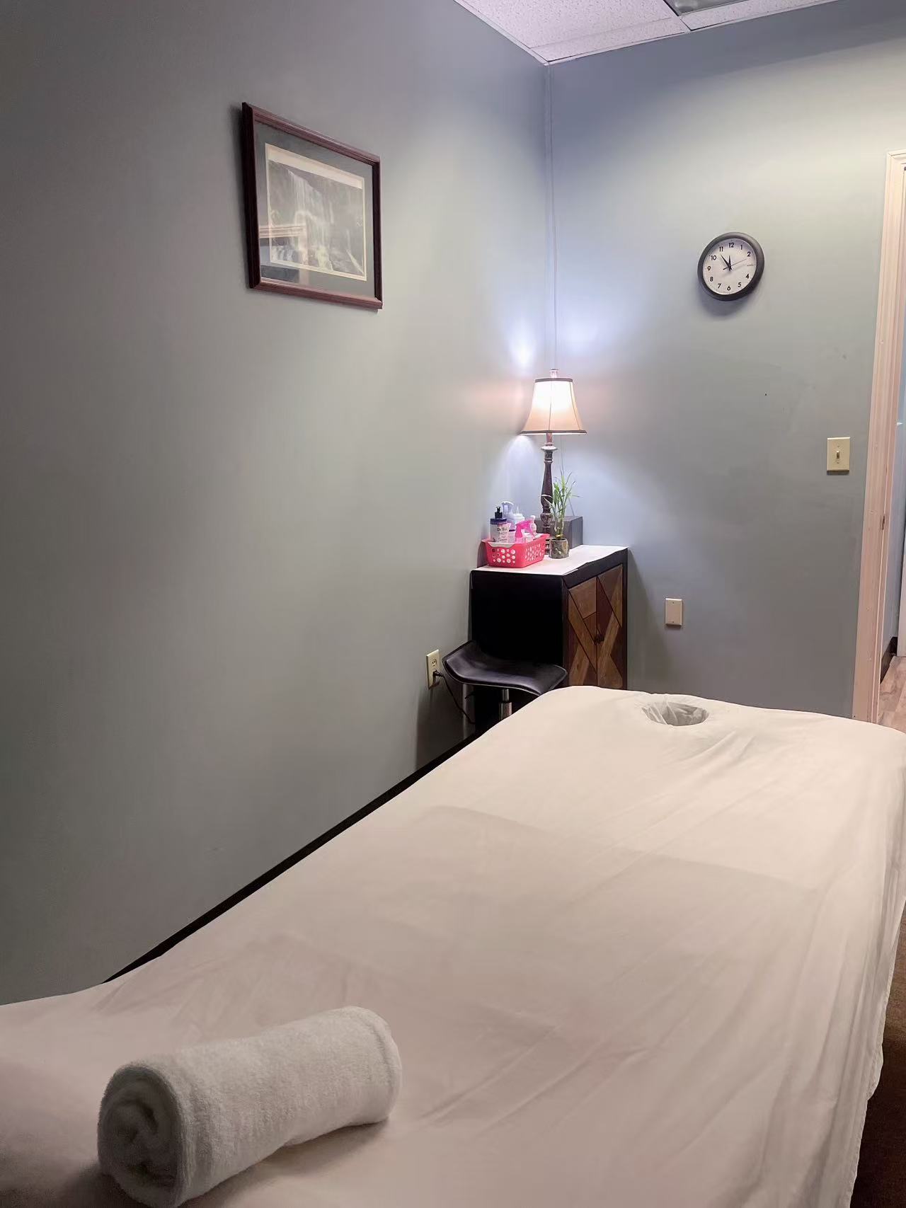 A treatment room with a massage table, lamp and framed waterfall picture